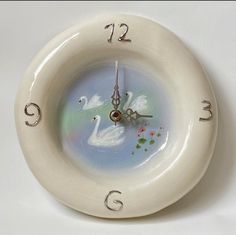 a white clock with two swans on it's face and numbers in the middle