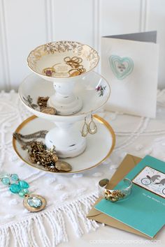 three tiered trays holding jewelry and cards on top of a white tablecloth