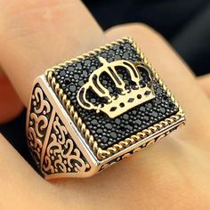 a gold and black ring with a crown on it's middle finger, sitting on someones hand