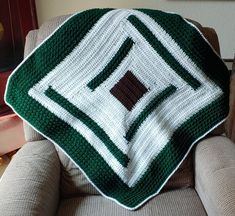 a green and white afghan sitting on top of a chair next to a pillow in the shape of a square