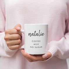 a person holding a coffee mug with the words natalie on it in black writing, while wearing a pink sweater