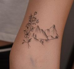 a tattoo with mountains and flowers on the back of her arm is shown in black ink