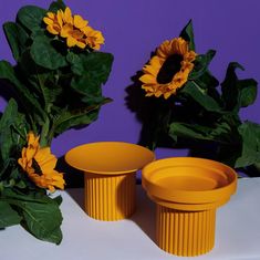 two yellow vases sitting next to each other with sunflowers in the background