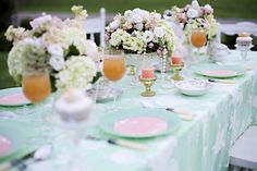 the table is set with pink and white flowers in vases, plates and glasses