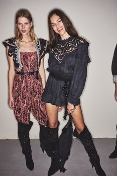 two women standing next to each other in front of a white wall wearing black boots