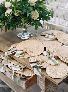 a wooden table topped with lots of plates covered in paper and greenery next to a vase filled with white flowers