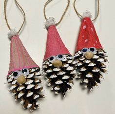 three pine cones with googly eyes are hanging from twine strings on a white surface