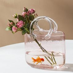 a vase filled with water and flowers on top of a white table next to a goldfish