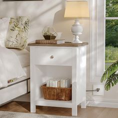 a white night stand with a basket on it next to a bed and a window