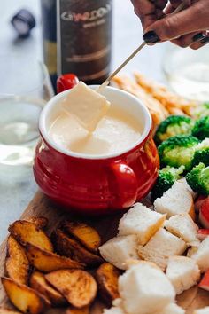 a person dipping cheese into a bowl with broccoli and other food on the side