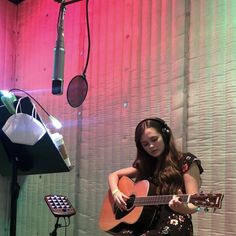 a woman sitting in front of a microphone and playing an acoustic guitar with headphones on