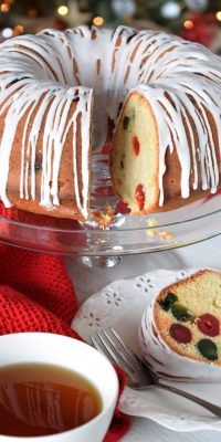 a bundt cake with white icing sitting on top of a table next to a cup of tea