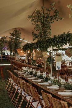 tables and chairs are set up under a tent for an outdoor wedding reception with greenery