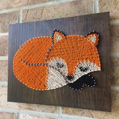 an orange and white fox is on a brown wood plaque with beaded string work