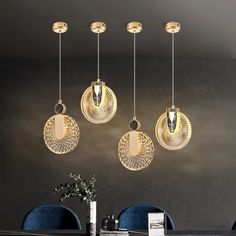 three circular lights hanging from the ceiling above a dining room table with blue chairs and black walls