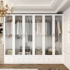 a white closet with lots of clothes hanging on the doors and drawers, in front of a chandelier