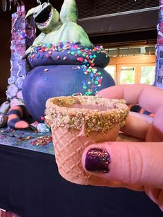 a hand holding an ice cream cone with sprinkles on it and a monster statue in the background