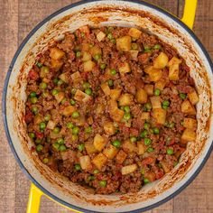 a pot filled with meat and peas on top of a wooden table next to a yellow napkin