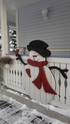 a snowman on the front porch of a house with red scarf and black hat