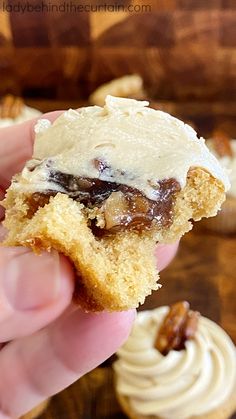 a hand holding a half eaten cookie with white frosting and walnuts on top