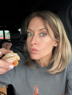 a woman holding food in her hand while sitting in the back seat of a car