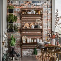 an outdoor dining area with brick wall and potted plants on the shelves above it