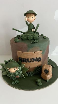 a cake with a boy on top of it and soldiers in the back ground behind him