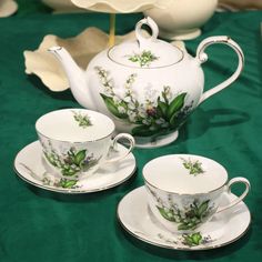 three tea cups and saucers on a green table cloth with flowers painted on them