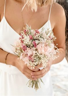 a woman wearing a white dress holding a bouquet of pink and white flowers in her hands