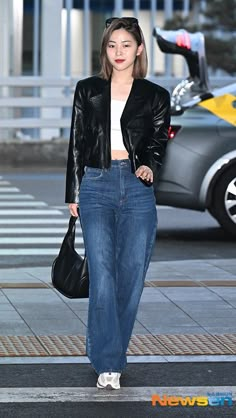 a woman in jeans and a black jacket is walking down the street with her hand on her hip