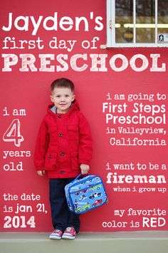 a little boy standing in front of a red wall with his back to school bag