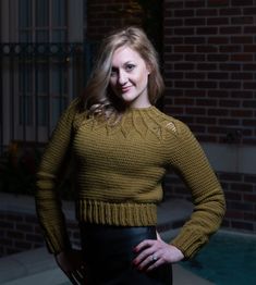 a woman standing in front of a pool wearing a brown sweater and black leather skirt