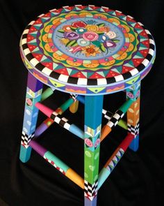 a brightly colored stool made out of crayons on a black background, with an artistic design painted on the top