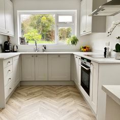 a kitchen with white cabinets and wood flooring is pictured in this image, there are plants on the window sill