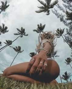 a woman is sitting in the grass with her hands on her knees and palm trees behind her