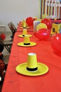 there are many hats and balloons on the long table with red tables cloths that have been set up for an event