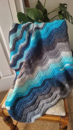 a crocheted blanket sitting on top of a wooden chair next to a potted plant