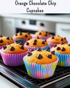 orange chocolate chip cupcakes sitting on top of a cooling rack in front of an oven