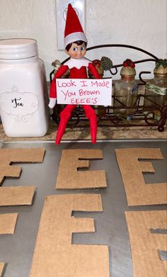 an elf sitting on top of a table holding a sign