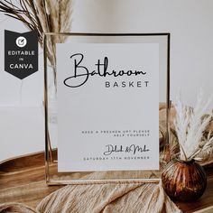 a bathroom basket sign sitting on top of a wooden table next to a vase filled with dry grass