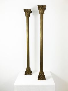 two tall gold vases sitting on top of a white pedestal