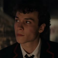 a young man with curly hair wearing a suit and tie looking at the camera while staring into the distance