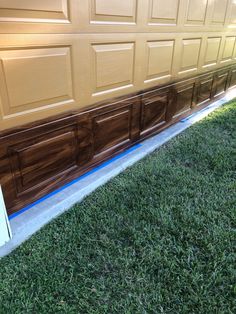 a brown garage door with blue tape on the side and grass in front of it