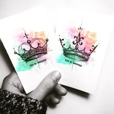 two cards with watercolor designs are being held in front of each other by someone's hand