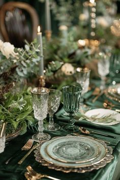 the table is set with green and gold plates, silverware, and greenery