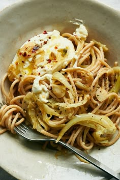 a white bowl filled with pasta and topped with an egg on top, next to a fork