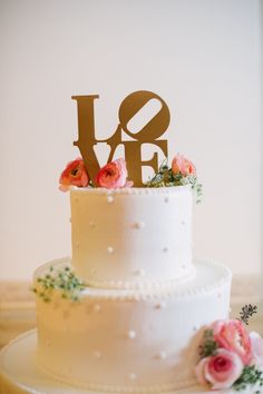 a white wedding cake with pink flowers and the word love on top