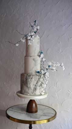 a three tiered white cake with blue flowers on the top and marbled stand