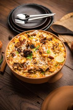 a bowl filled with food sitting on top of a wooden table next to plates and utensils