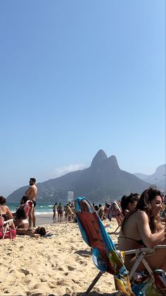 many people are sitting on the beach with mountains in the background